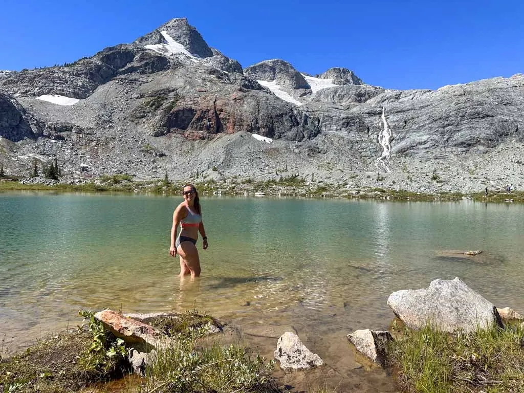A hiker swimming in an alpine like with a mountain and glacier in the background