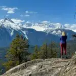 A woman stands on a bluff near Brohm Lake with snowy mountains in the distance. Get everything you need to know to hike at Brohm Lake
