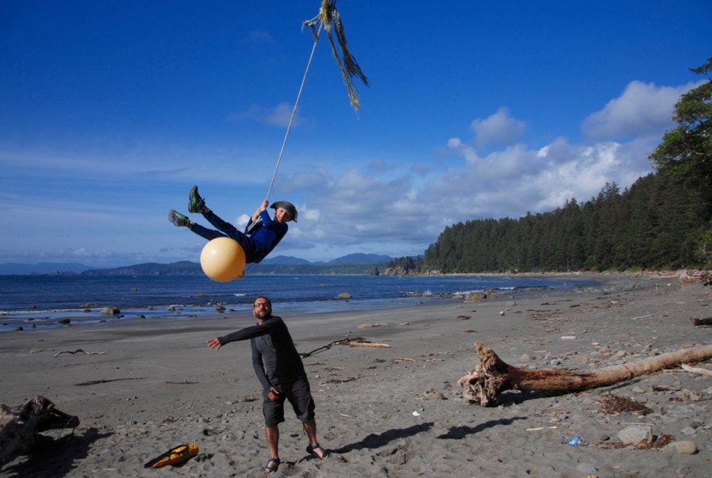An adult pushes a boy on a rope swing on the beach of the Ozette Loop Trail