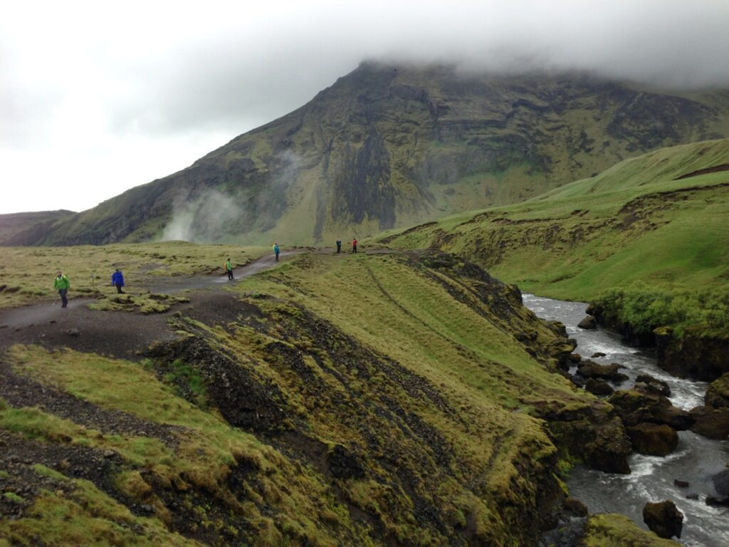 Hikers wearing rain jackets hike in rain and fog near Skogafoss in Iceland