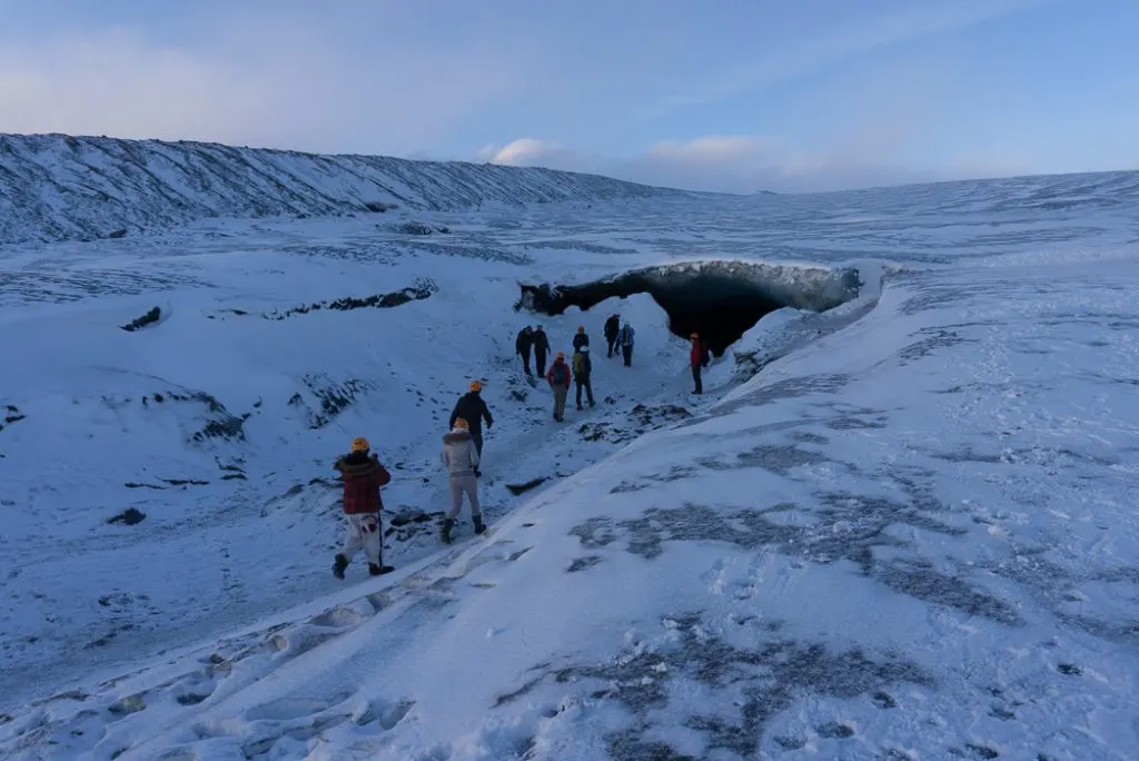A tour group makes their way towards the mouth of an ice cave in Iceland. The Ultimate Guide to Ice Caves in Iceland: Everything you ever needed to know about visiting ice caves in Iceland. Find out how to go INSIDE the Crystal Cave glacier ice cave to see the blue ice.