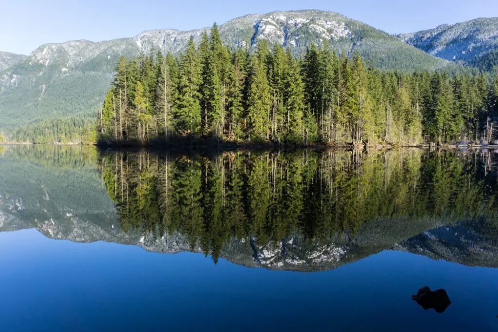 Mountains reflected in a lake on a quiet hiking trail. Don't like crowds? Here are 15 ways to avoid crowded hiking trails.