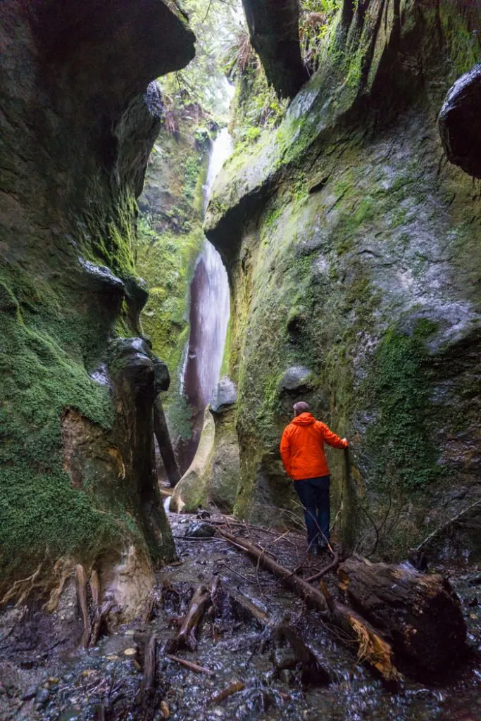 A hiker explores a hidden waterfall inside a canyon near Sombrio Beach on the Pacific Marine Circle Route