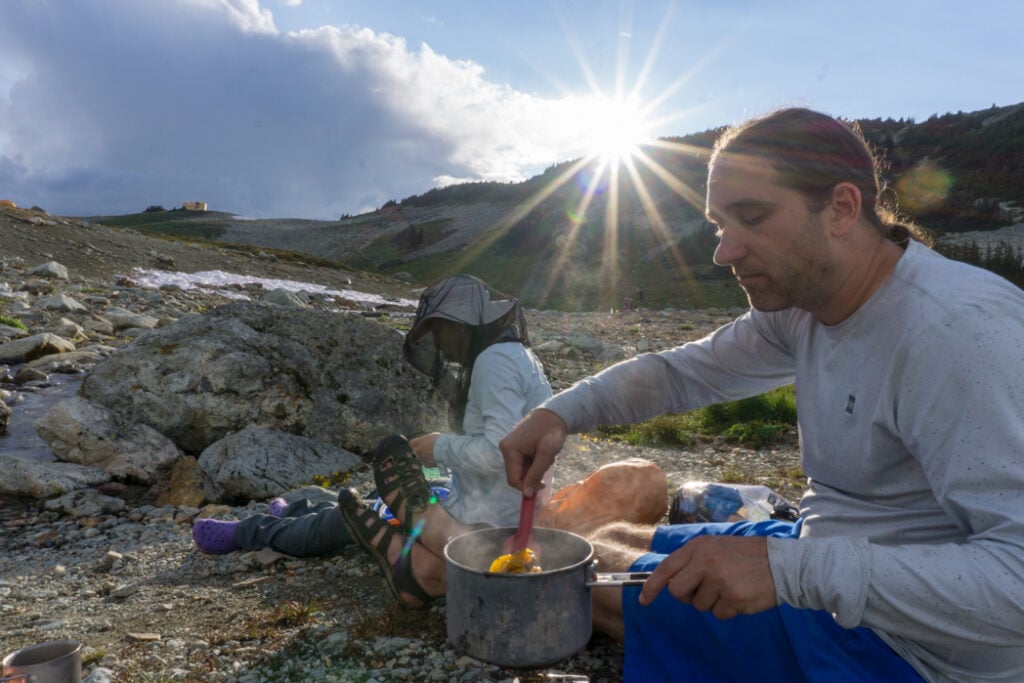 Person cooking dinner on a camp stove on a backpacking trip. How to choose backpacking meals.