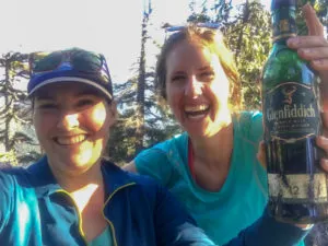 Two hikers with a bottle of whiskey found on a mountain top. Learn how to find hidden whiskey caches in the mountains of Vancouver in the book The Glorious Mountains of Vancouver's North Shore.