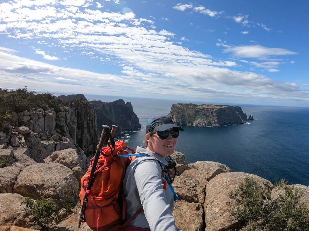 A hiker takes a selfie in front of the view of Tasman Island on the Cape Pillar Track in Tasmania