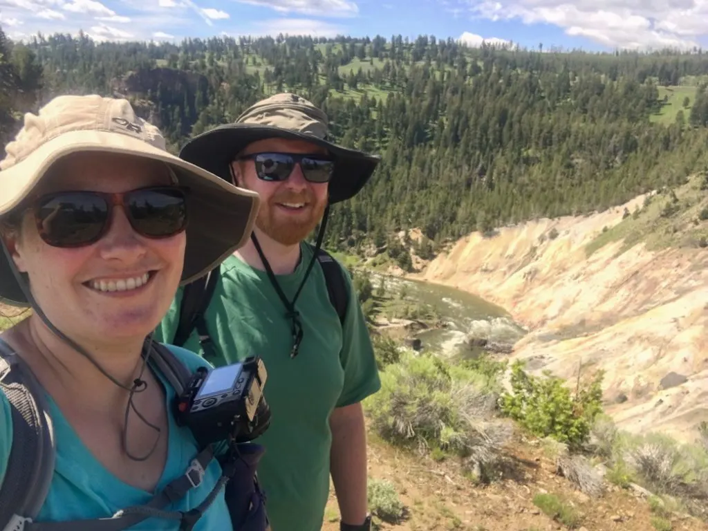 Two hikers wearing wide-brimmed hats and sunscreen in Yellowstone National Park. Make sure to put sun hats on your Yellowstone packing list.