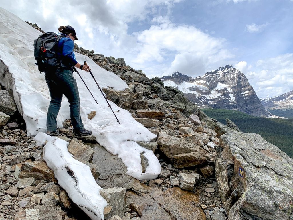 A hiker walking through snow with trekking poles on the All Soul's Alpine Route at Lake O'Hara in Yoho National Park