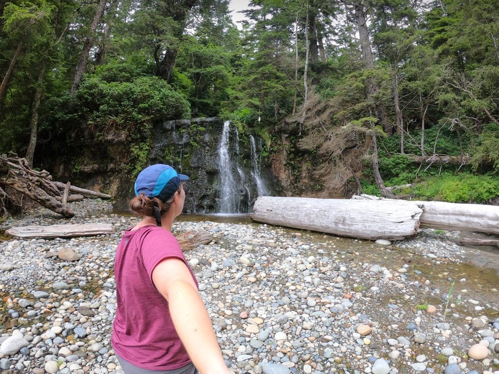 A hiker in front of a waterfall on the West Coast Trail