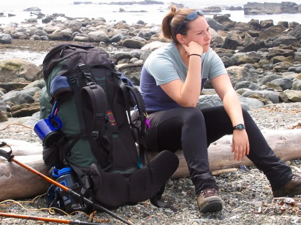 A hiker sits next to her backpack on her first backpacking trip