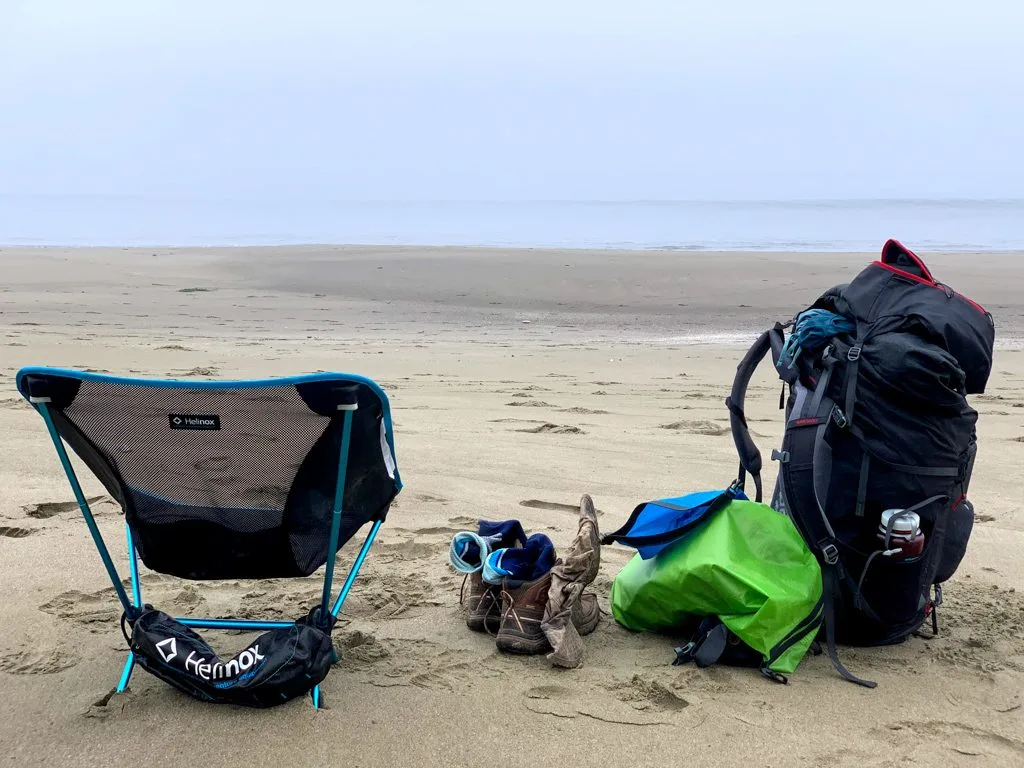 A backpacking chair on the beach next to a backpacking pack