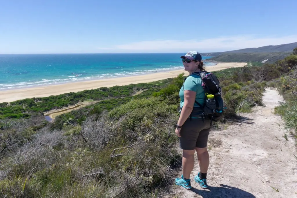 Female hiker wearing a backpack on a trail near the ocean in Narawantapu National Park in Tasmania, Australia