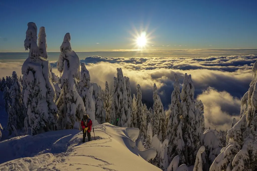 A snowshoer stands on top of a peak above the clouds