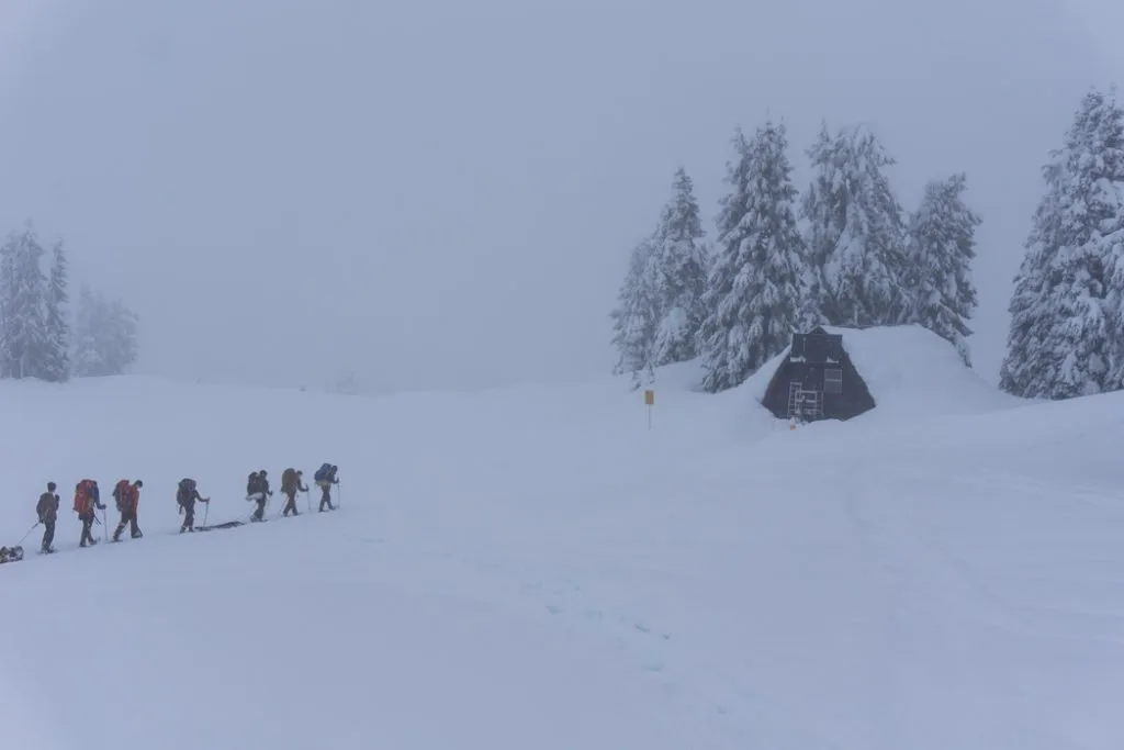 A group of snowshoers walking through a snowstorm and fog to reach a backcountry hut. Learn how to avoid getting caught in a storm to improve your snowshoeing safety