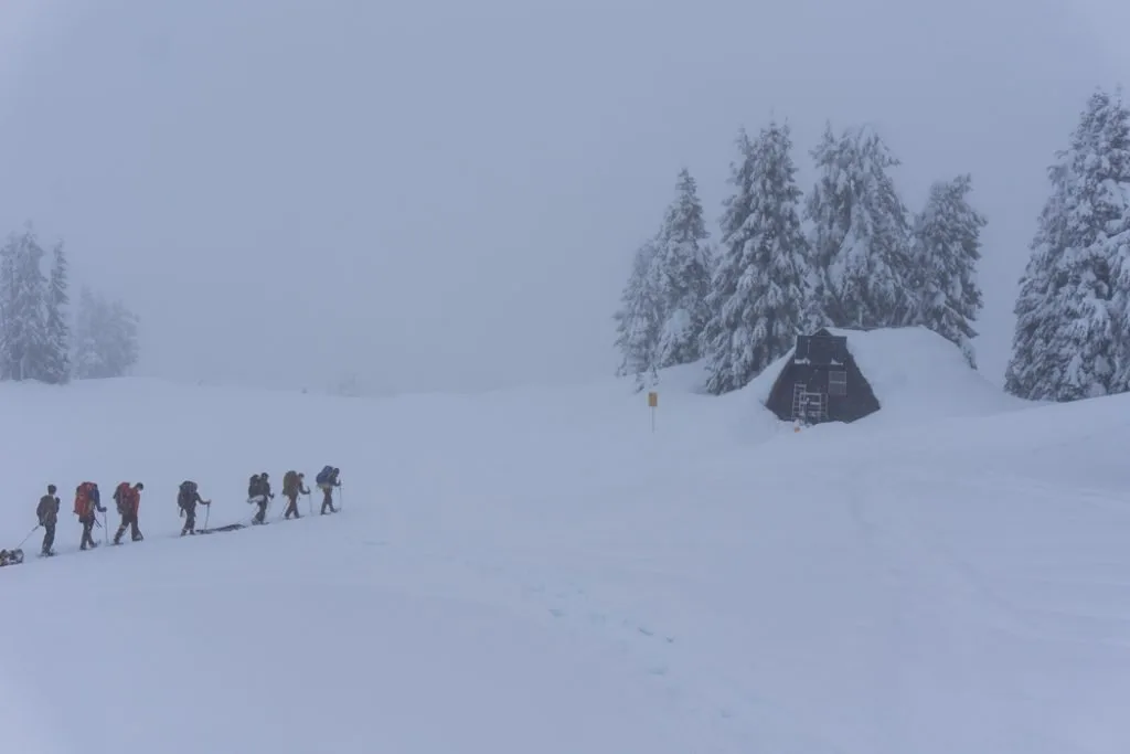 A group of snowshoers walking through a snowstorm and fog at Elfin Lakes Shelter.