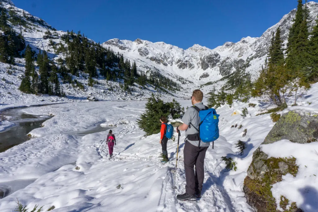 Hikers cross a snowy valley with some open water in a stream