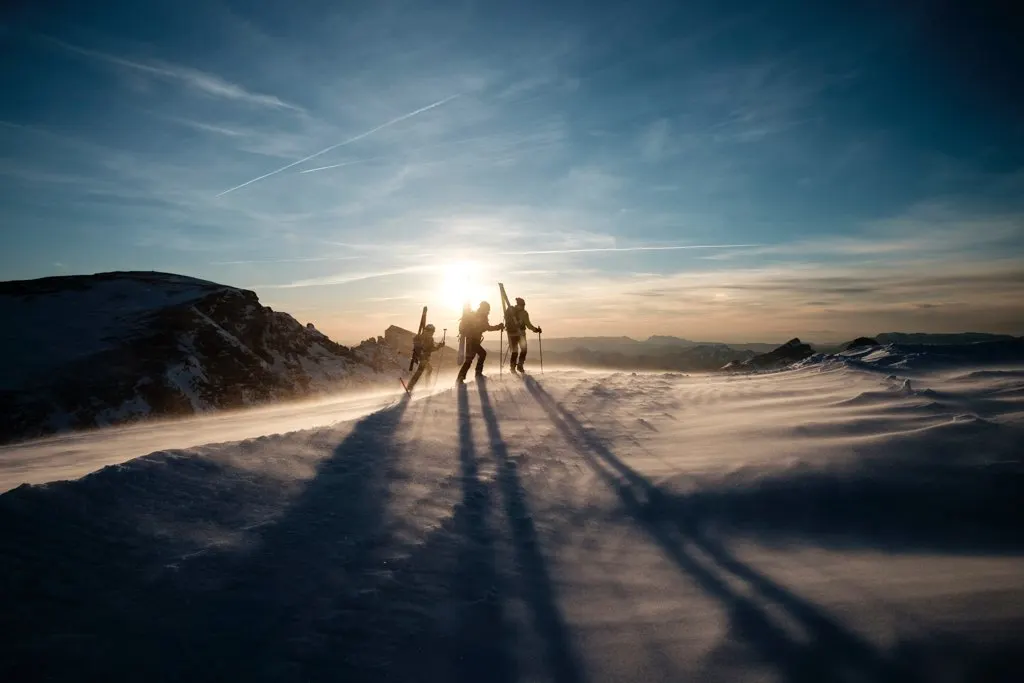 Three people ski touring as the sun sets