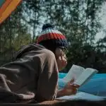 A woman reading a book in a tent. Get recommendations for the best women's adventure books from this list