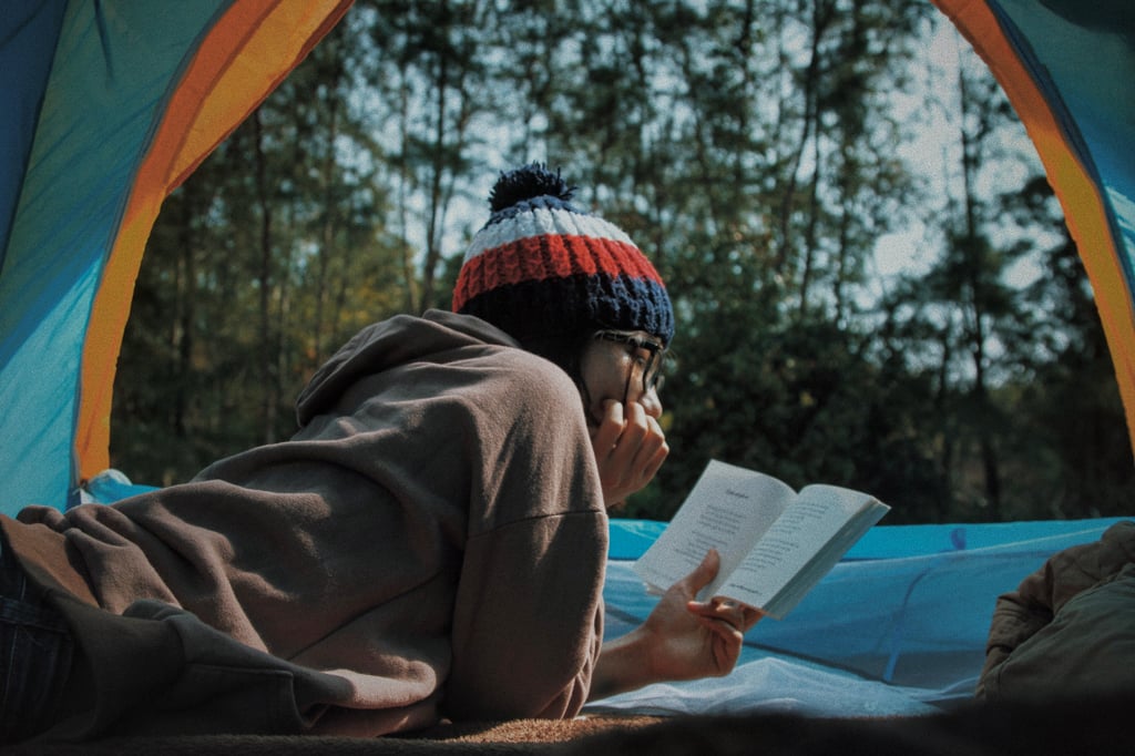 A woman reading a book in a tent. Get recommendations for the best women's adventure books from this list