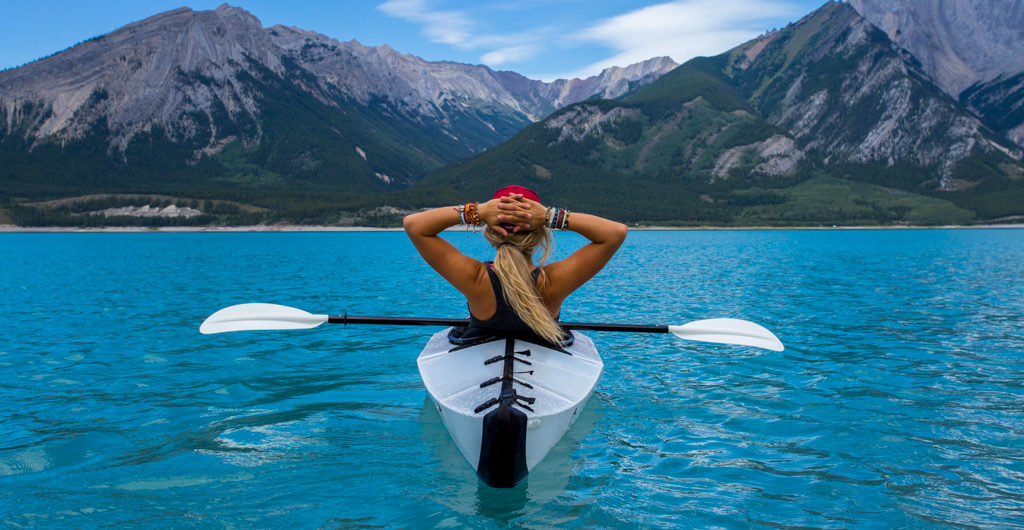 A woman sits in a kayak on a blue lake. Watch women's adventure films.