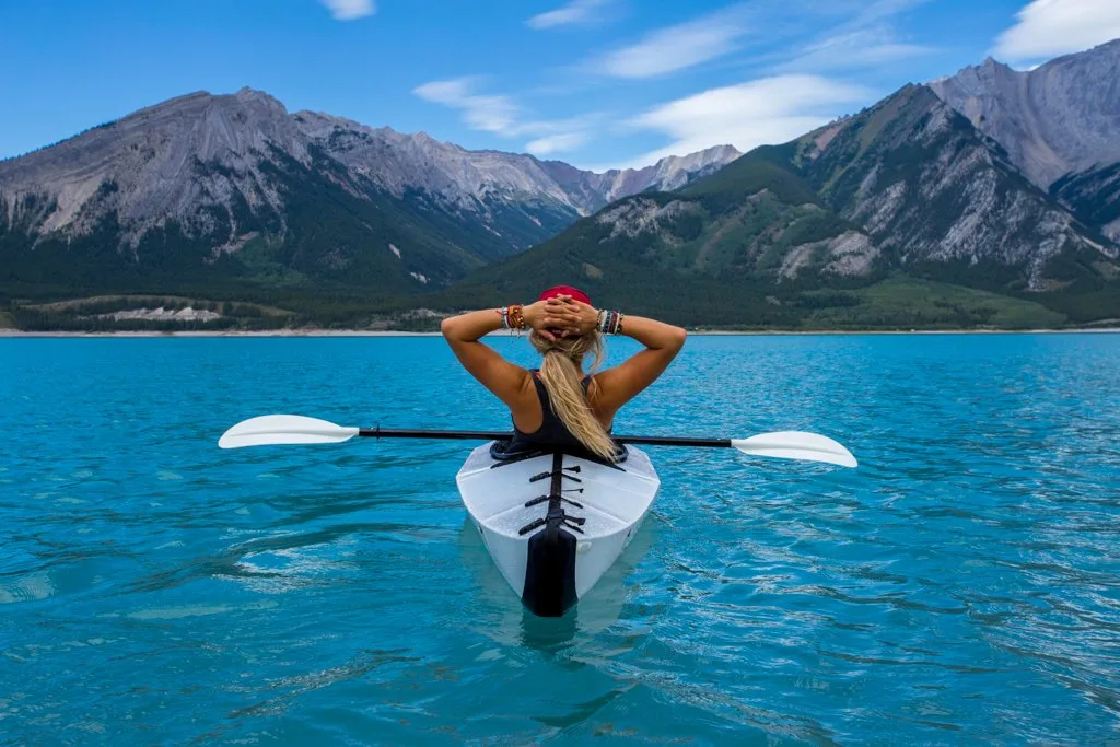 A woman sits in a kayak on a blue lake. Watch women's adventure films.