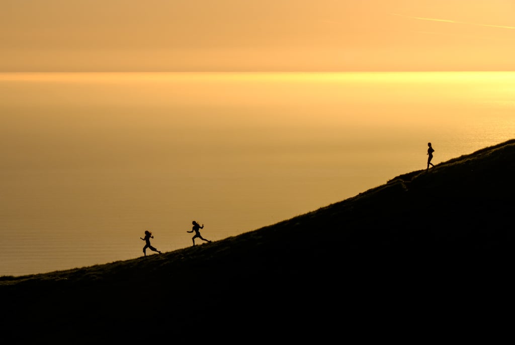 The silhouettes of three women as they run down a hill at sunset. Get this list of women's adventure films about running.