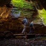 Two hikers walk along a boardwalk into Bear Gulch Cave in Pinnacles National Park in California