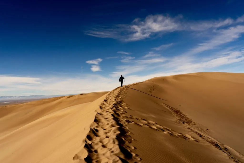 A hiker walks up a sand dune against a blue sky in Great Sand Dunes National Park in Colorado