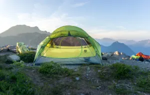 A tent on top of a mountain ridge with mountains in the background. A backpacking tent is one of the basic items on your backpacking checklist - things you should pack for a backpacking trip