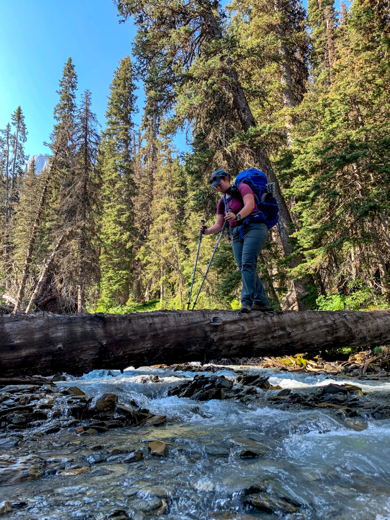 A hiker crossing a log over Numa Creek on the Rockwall Trail