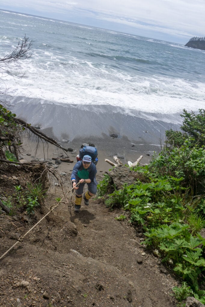 A hiker ascending a fixed rope in Olympic National park. Get tips for coastal hiking before you try this tough trail