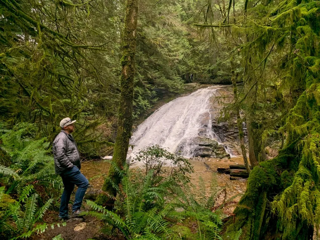 A man stands looks at a waterfall from a hiking trail in Cliff Gilker Park near Roberts Creek on the Sunshine Coast, BC