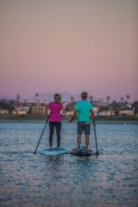 A couple holds hands as they paddleboard at sunset. One of the best Valentine's gifts for hikers and campers - vouchers for paddleboard lessons.