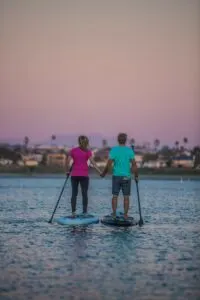 A couple holds hands as they paddleboard at sunset. One of the best Valentine's gifts for hikers and campers - vouchers for paddleboard lessons.