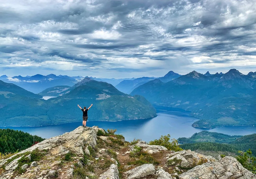 A woman standing at the peak of Tin Hat Mountain on the Sunshine Coast Trail - one of the best places to go backpacking in BC without a car