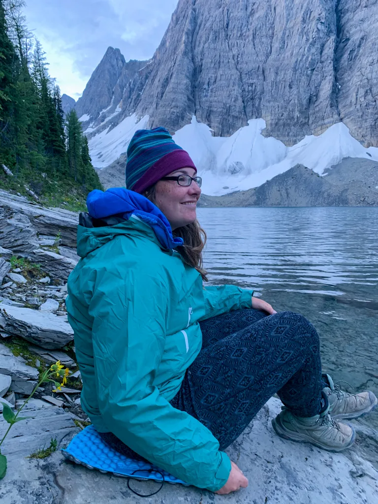 A woman sitting on the shoreline of Floe Lake on the Rockwall Trail
