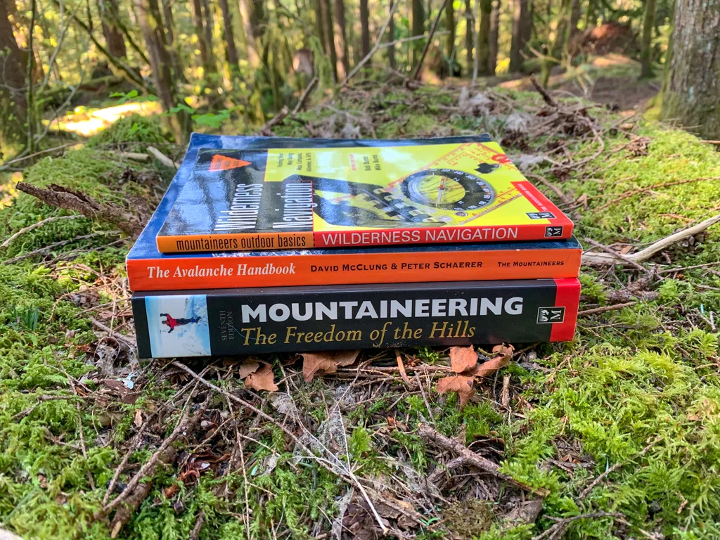 Three outdoor skills and wilderness education books for hikers stacked on moss