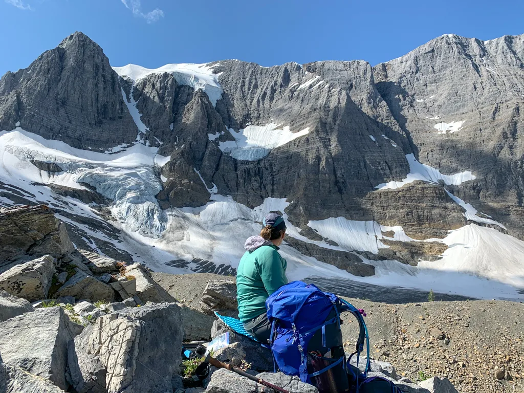 A woman sitting down next to a backpack and looking at a glacier on the Rockwall Trail
