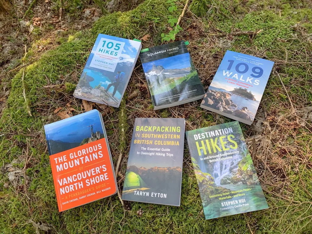 Six Vancouver hiking guidebooks spread across moss