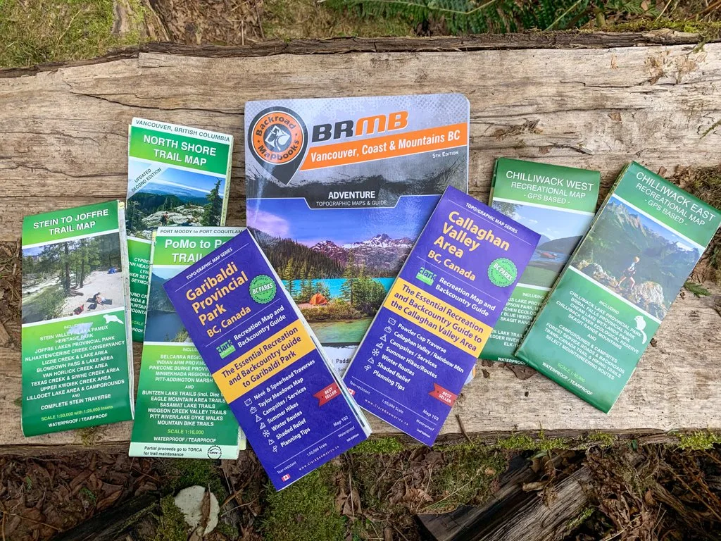 Several Vancouver hiking maps spread across a log