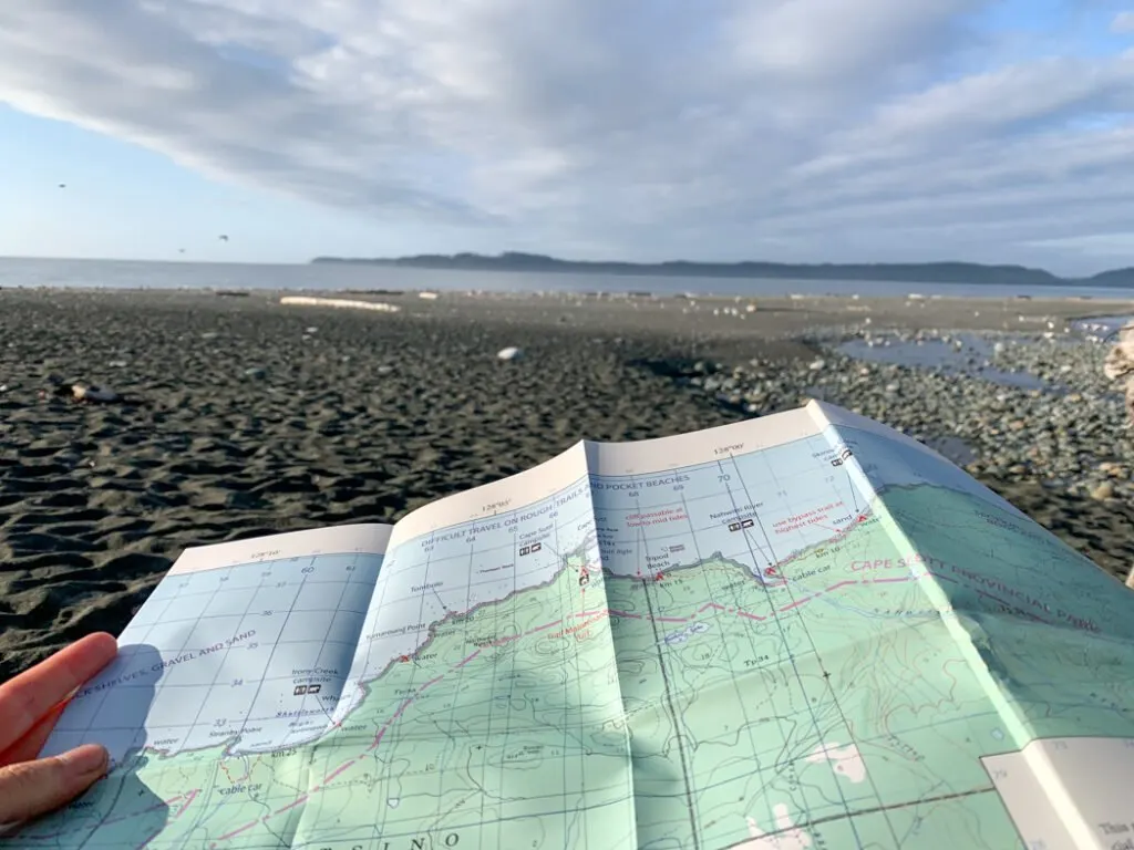 A hiker hold a map on a beach hike - Navigation is a key skill for backpacking