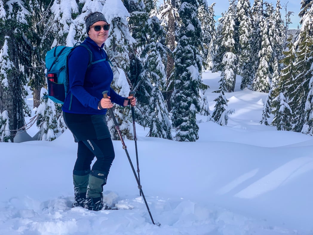 A woman wearing an insulated skirt snowshoes through a snowy forest