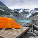 An orange tent in front of Wedgemount Lake and snow covered mountains near Whistler. One of the best bakcpacking trips in BC