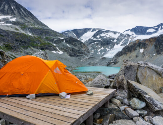 An orange tent in front of Wedgemount Lake and snow covered mountains near Whistler. One of the best bakcpacking trips in BC