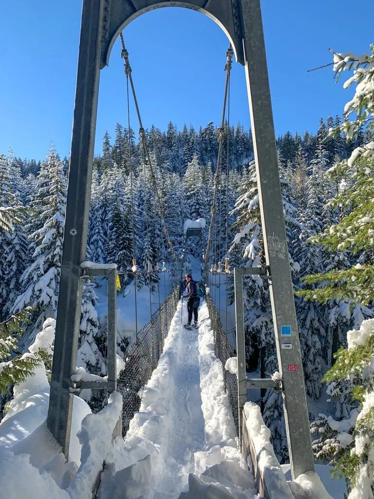 A woman snowshoes across a suspension bridge over the Cheakamus River in Whistler