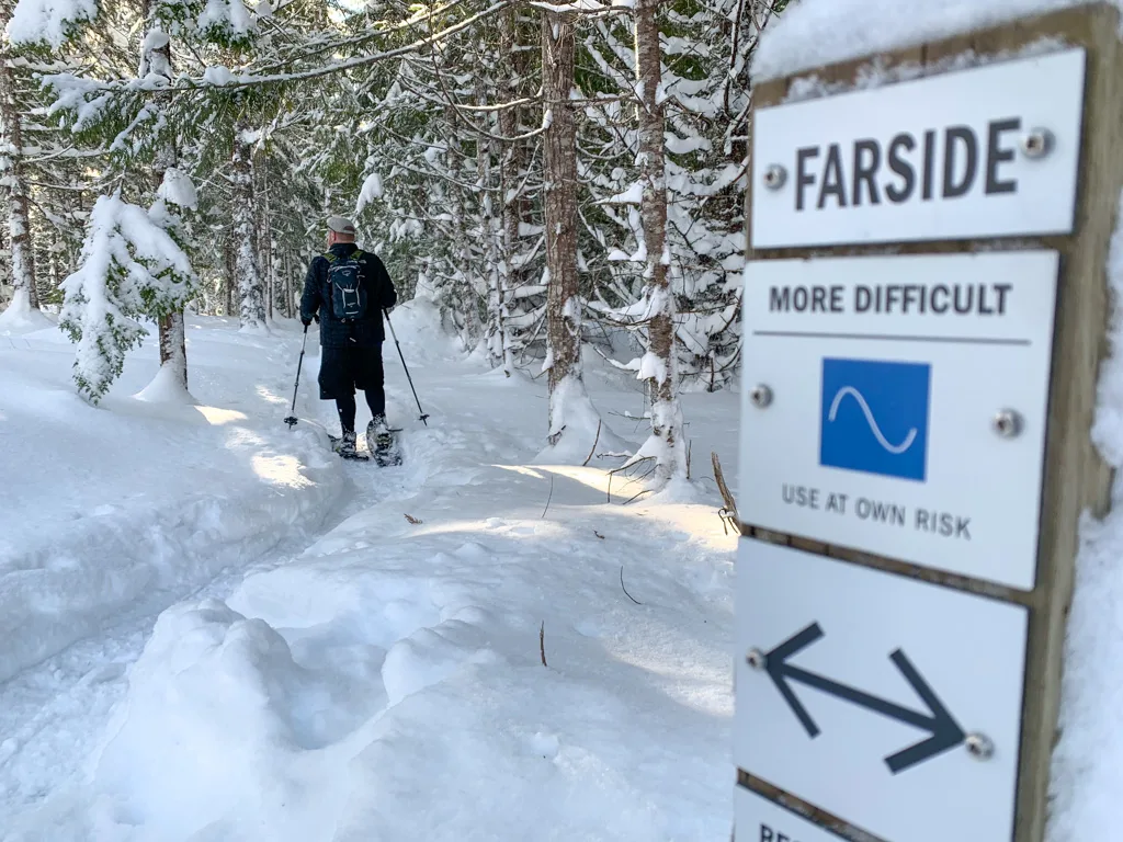 A man snowshoes past a trail sign on the Farside Trail by the Cheakamus River in Whistler