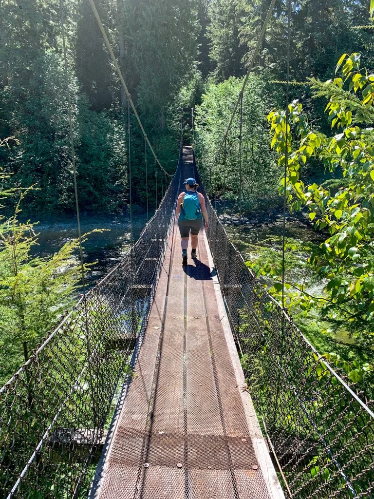 A female hiker wearing shorts and backpack walks across the Cal-Cheak Suspension bridge at the Cal-Cheak Campground in Whistler