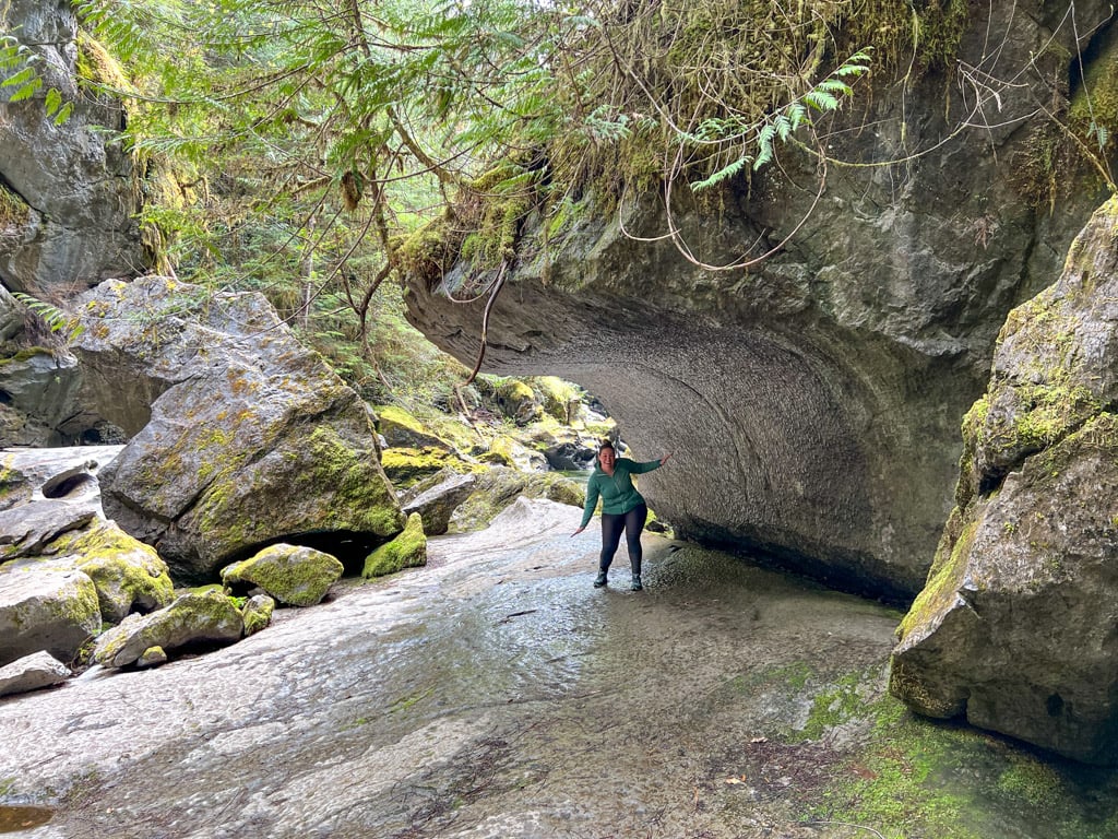 A hiker posing under an overhanging rock formation near Little Huson Caves.