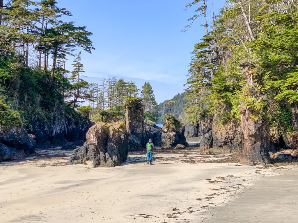 A male hiker wearing a green backpack hikes past sea stacks at San Josef Bay in Cape Scott Provincial Park on Northern Vancouver Island