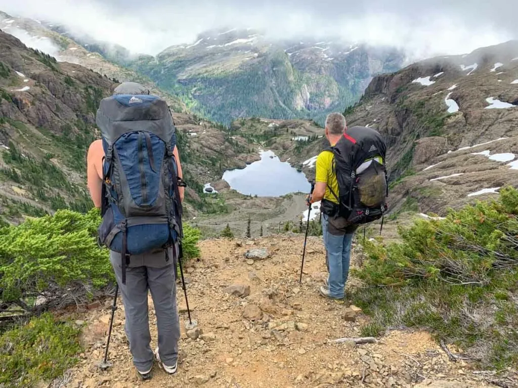 Two hikers in front of a view of cloudy mountains and a lake - they need the best weather apps for hiking